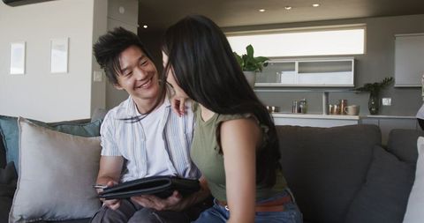 Young couple smiling reviewing portfolio on gray sofa in modern open-plan apartment