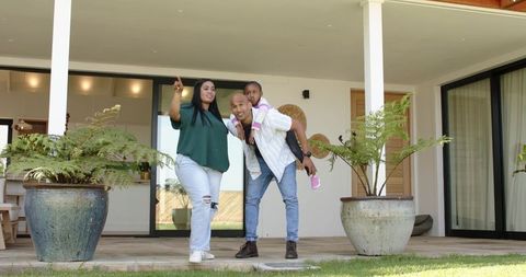 Diverse family standing on modern porch pointing and carrying child, family lifestyle moment