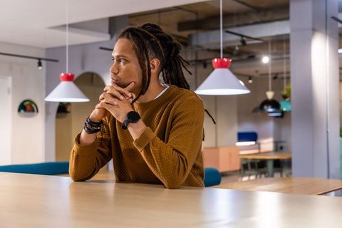African American man sitting in modern coworking space wearing smartwatch and thinking