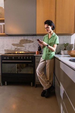 Asian woman leaning on kitchen counter checking smartphone in modern minimalist kitchen