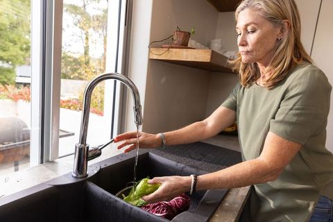 Senior Woman Washing Fresh Greens at Kitchen Sink in Bright Culinary Space