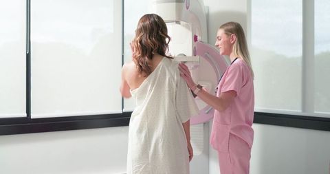 Female patient receiving mammogram from technician in pink scrubs during breast screening