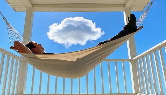 Reclining man in hammock on sunlit porch under single fluffy cloud