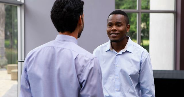 Two African American men engage in a conversation outdoors, with copy space. They appear to be young professionals, colleagues, having a discussion in a casual work setting.