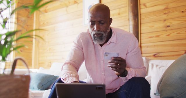 Senior african american man in log cabin using tablet and holding credit card. Log cabin and lifestyle concept.