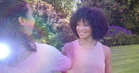 Smiling woman receiving reassuring shoulder touch in garden with pastel lens flare