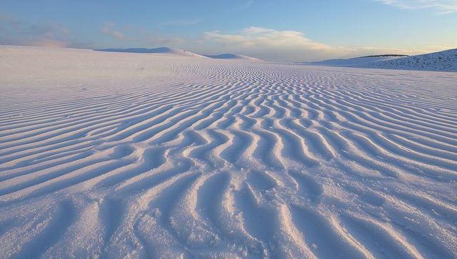 Rippling white sand dunes stretching toward sunrise across vast serene landscape