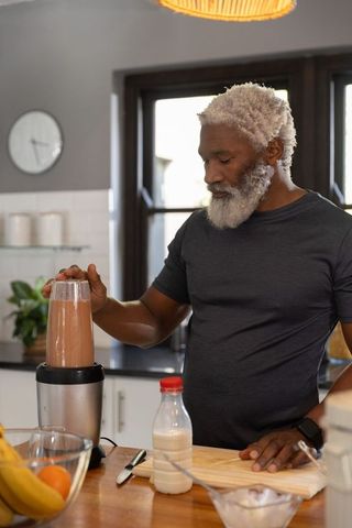 Mature african american man preparing chocolate smoothie in bright home kitchen morning