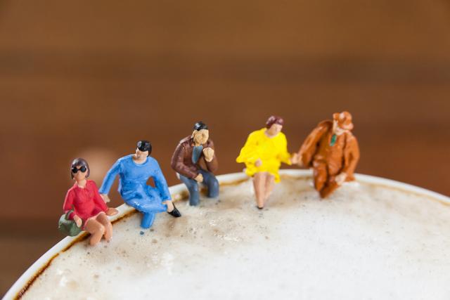 Miniature figures of friends sitting on coffee foam, symbolizing socializing and togetherness. Ideal for use in concepts related to friendship, coffee culture, social gatherings, and creative advertising.