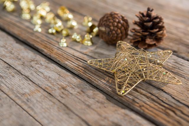 Golden star, pine cones, and bells arranged on rustic wooden plank, perfect for holiday-themed designs, greeting cards, festive invitations, and seasonal marketing materials.
