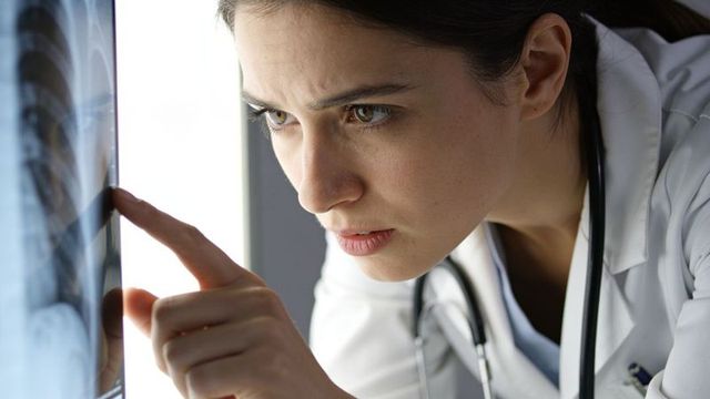 Female doctor examining chest x-ray on lightbox, pointing at radiograph, focused