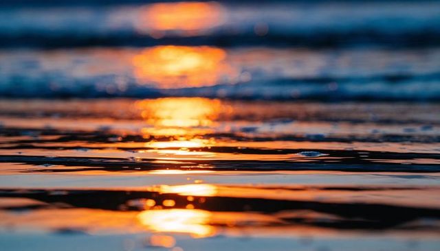 Sunset light reflecting on shallow sea and wet sand with golden bokeh ripples