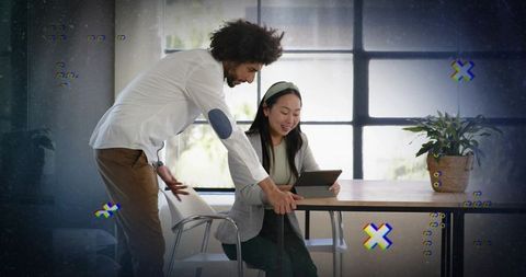 Man leaning and guiding female colleague using tablet for teamwork and collaboration in modern offic
