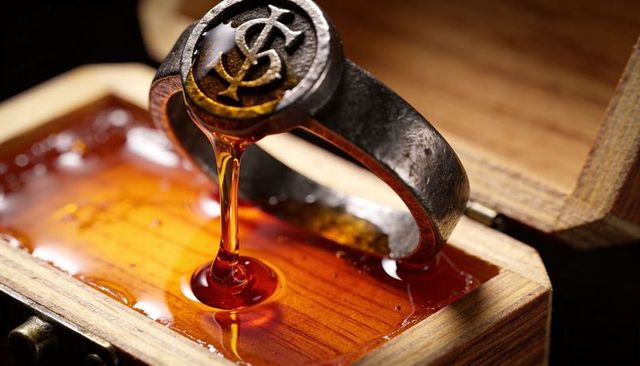 Dripping signet ring releasing amber resin into wooden jewelry box, vintage monogram