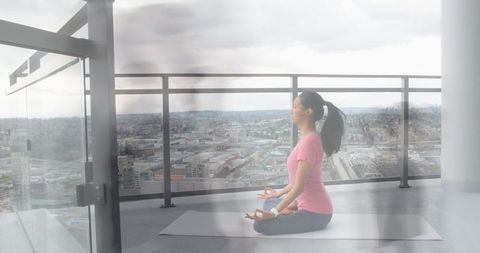 Asian Woman Meditating on Balcony Overlooking Cityscape