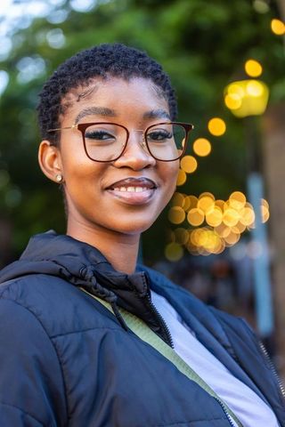 African american woman smiling in glasses quilted jacket urban twilight with bokeh lights