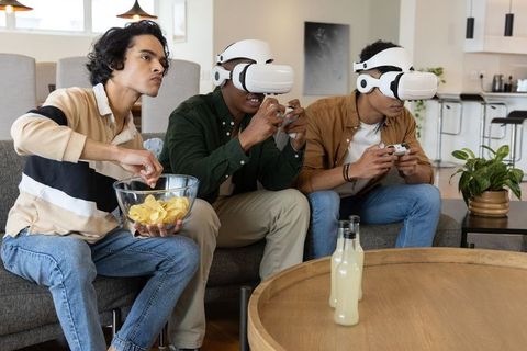 Three friends playing vr multiplayer at home wearing headsets and holding controllers