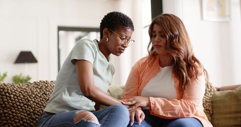 Diverse women comforting on sofa in bright living room offering emotional support
