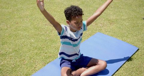 Young Boy Practicing Yoga Outdoors on Blue Mat Under Sunlight
