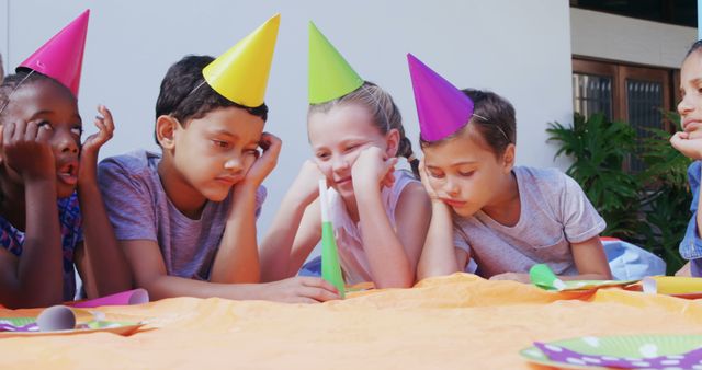 A group of diverse children wearing party hats appear bored or uninterested at a birthday celebration, with copy space. Their lack of enthusiasm contrasts with the festive setting, suggesting a lull in the party activities.