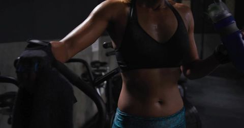 Sweaty woman leaning on spin bike holding towel and water bottle after intense cardio