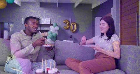 Couple celebrating 30th birthday on cozy sofa sharing cake and candles at home party