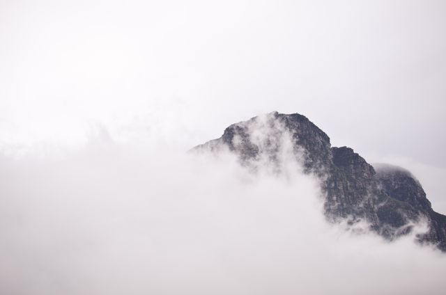 Mountain peak enveloped by misty clouds on a gloomy day. Ideal for nature-centric projects, travel blogs, and outdoor adventure promotions. Use it to evoke serenity, mystery, or the beauty of nature.