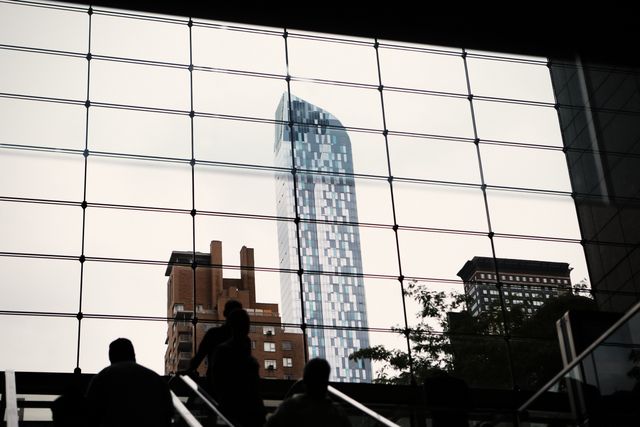 Capturing a contemporary skyscraper seen through the glass walls of a building, this image showcases the urban landscape, merging modern architecture with the everyday rhythm of city life. The shadows enhance the feeling of movement, making it suitable for use in corporate settings, real estate flyers, and architectural presentations that focus on innovative designs and cityscapes.
