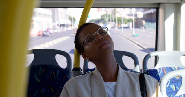 African american woman wearing glasses sitting in city bus sleeping. Transport, city living and lifestyle, unaltered.