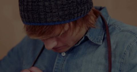 Young adult wearing blue beanie and denim shirt adjusting suspenders