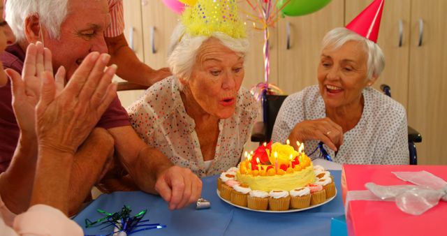 Elderly woman blowing out candles on a birthday cake surrounded by friends wearing party hats. Suitable for use in materials focusing on elderly care, senior lifestyle, celebrations, birthdays, and joyous occasions. Excellent for illustrating themes of community, happiness, and festivity in the lives of older adults.