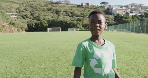 Boy Wearing Recycling T-shirt on Green Soccer Field Smiling Broadly with Copy Space