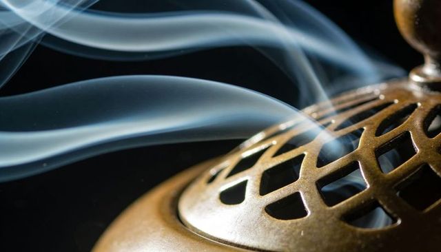 Bronze incense burner releasing curling smoke over dark backdrop for meditation rituals