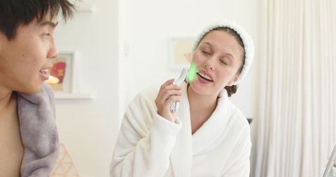 Couple sharing morning skincare ritual using led facial device and cozy white bathrobes