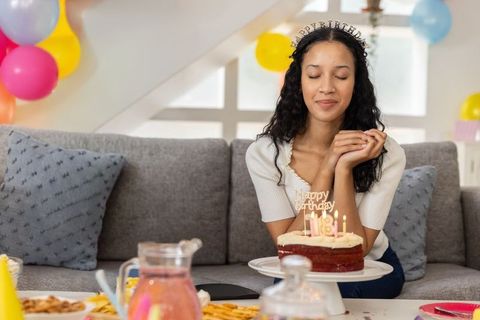 Teen girl celebrating birthday on gray sofa blowing out candles on red velvet cake