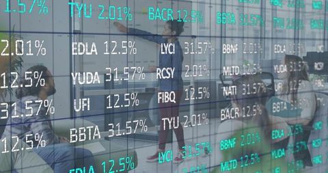 Presenting to team behind glass partition with financial ticker overlay and laptop