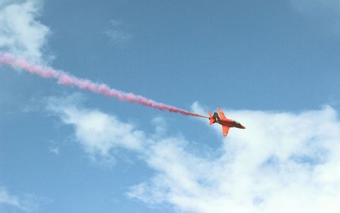 Red aerobatic plane with smoke trail in blue sky