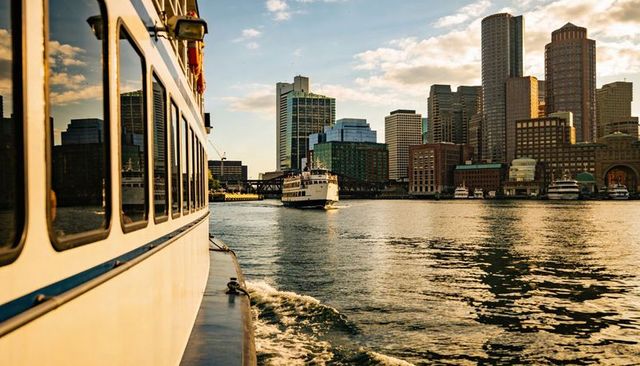 Ferry gliding through urban harbor at golden hour with skyline reflection and wake