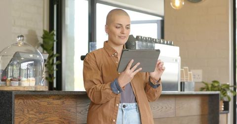 Smiling barista checking tablet behind cafe counter with cupcakes and espresso machine
