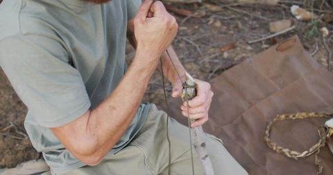 Wilderness survival tying rope to wooden stake man preparing camp shelter and gear
