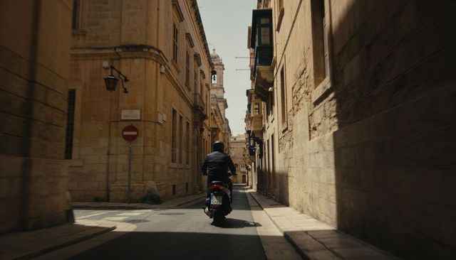Scooter rider cruising through sunlit narrow historic european alleyway with lanterns