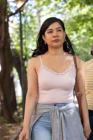 Woman walking in shaded park carrying brown shoulder bag wearing pink tank and tied sweater