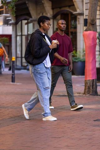 Friends walking on brick-paved shopping street holding takeaway coffee and backpack