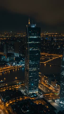 Drone capturing skyscraper spire and river under city lights vertical night skyline video