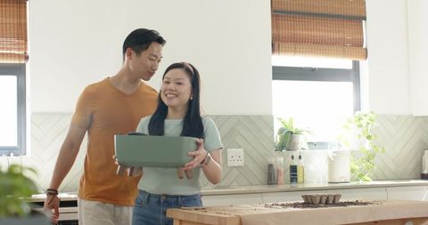 Asian couple planting seeds on kitchen island in sunlit modern home gardening lifestyle