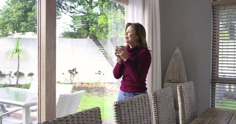 Mid adult woman enjoying morning coffee by sliding glass door overlooking backyard garden