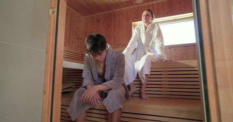 Mixed-race couple relaxing in wooden sauna wearing robes for spa wellness and serenity
