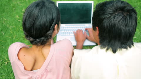 Couple using Laptop on Grass for Outdoor Relaxation
