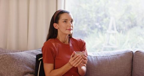 Woman Holding Mug Peacefully Seated on Sofa in Cozy Living Room