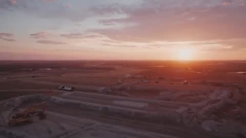 Drone footage capturing golden hour over open-pit quarry with excavator and haul trucks